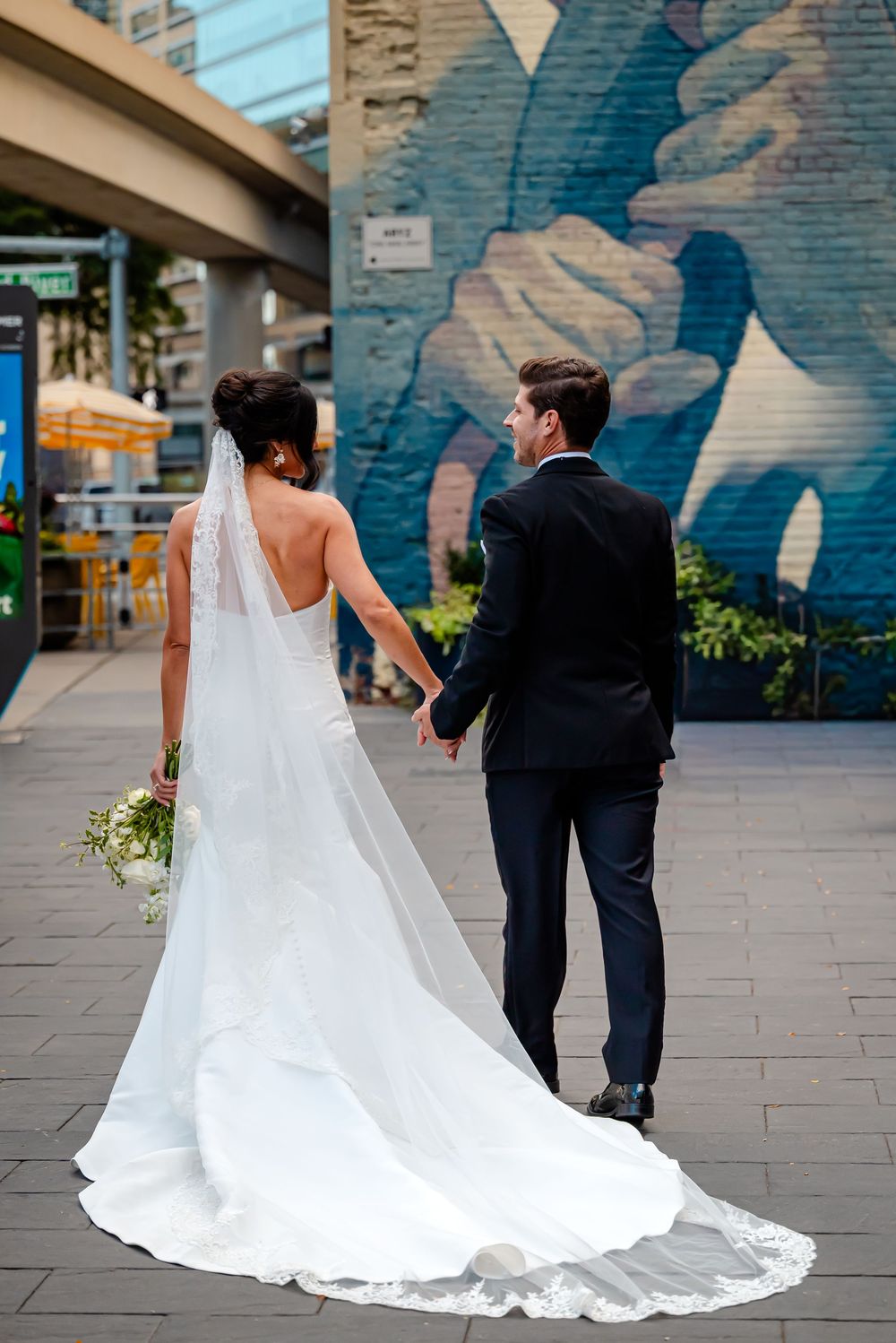 Wedding couple walking together against a blue urban mural backdrop with flowing white dress train.