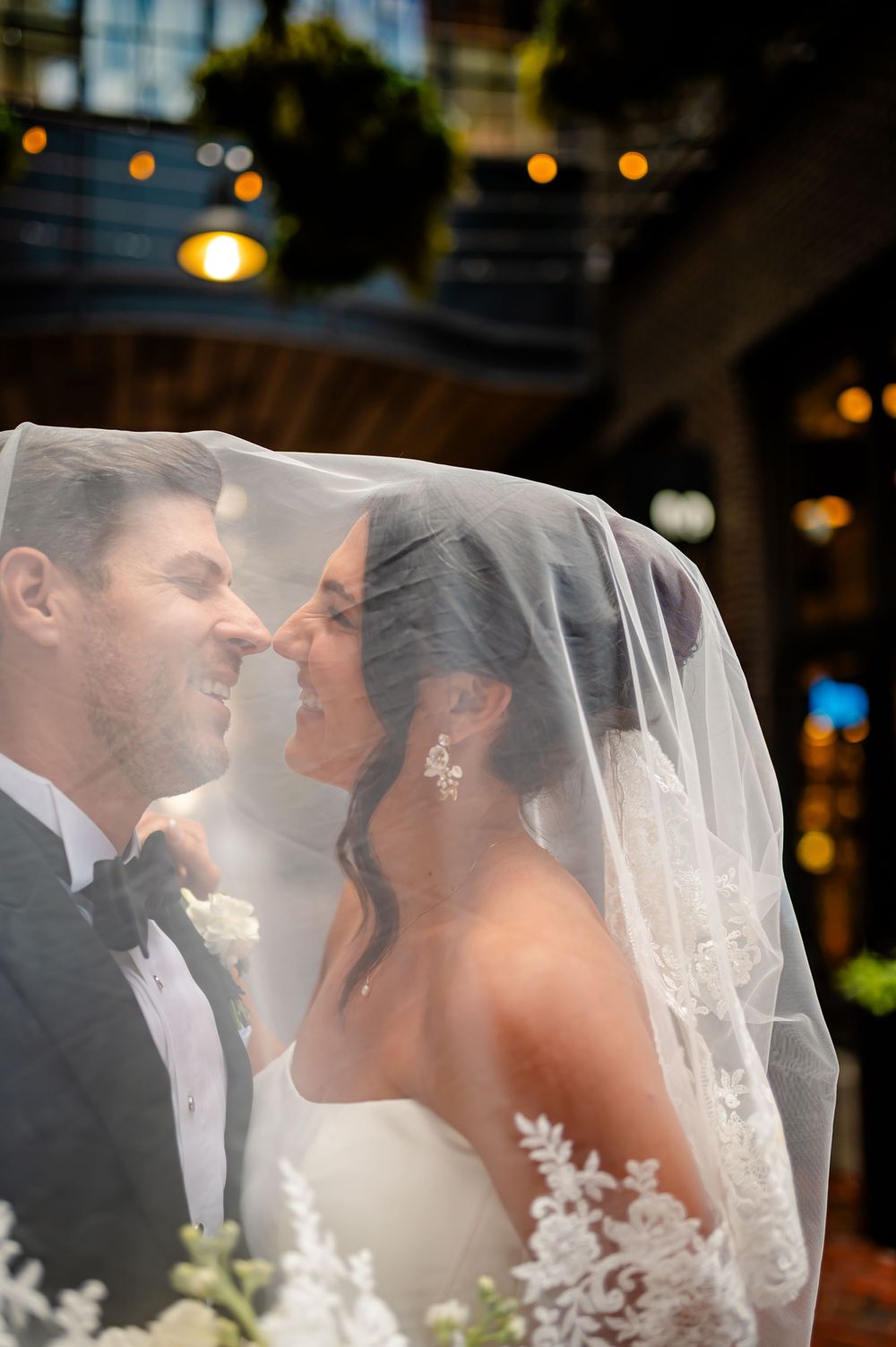 A romantic wedding couple shares a tender kiss under a flowing white veil during their celebration.