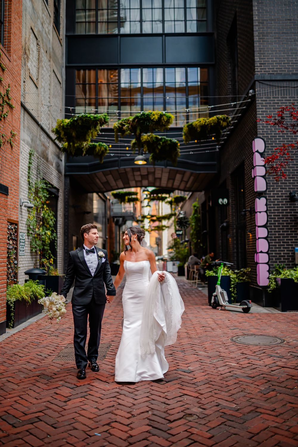 Couple walking along a charming brick-paved courtyard with hanging lanterns and industrial architecture.