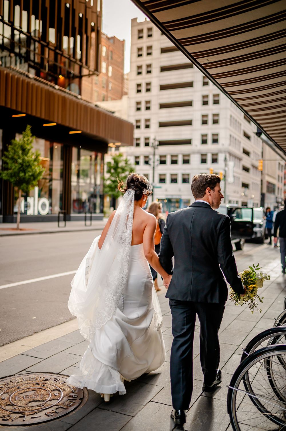A couple in wedding attire walks down a city street with a bicycle in view, captured in a sequence of photos.