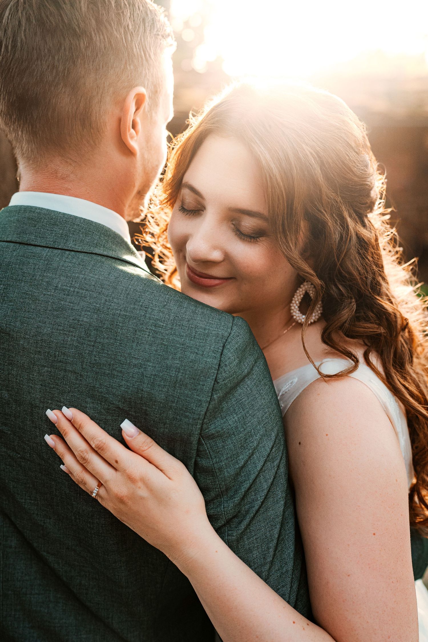 A romantic couple in white clothing shares an intimate moment in a wooded setting during golden hour.