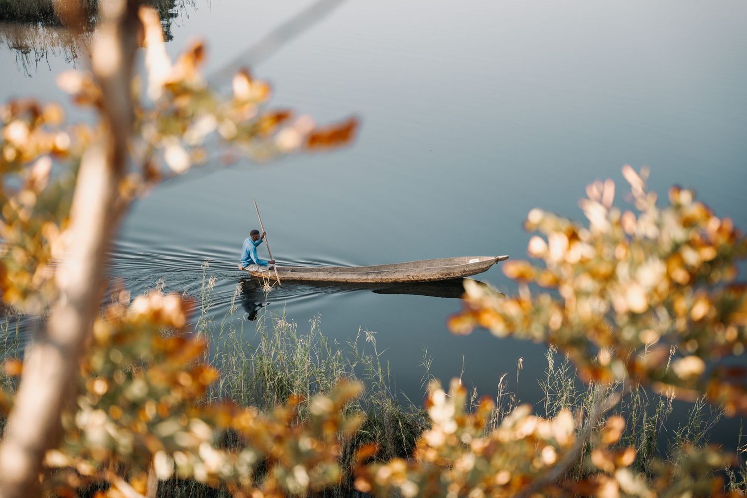 Scenic view of a lake with autumn foliage and silhouette of a person fishing from a boat in the distance.