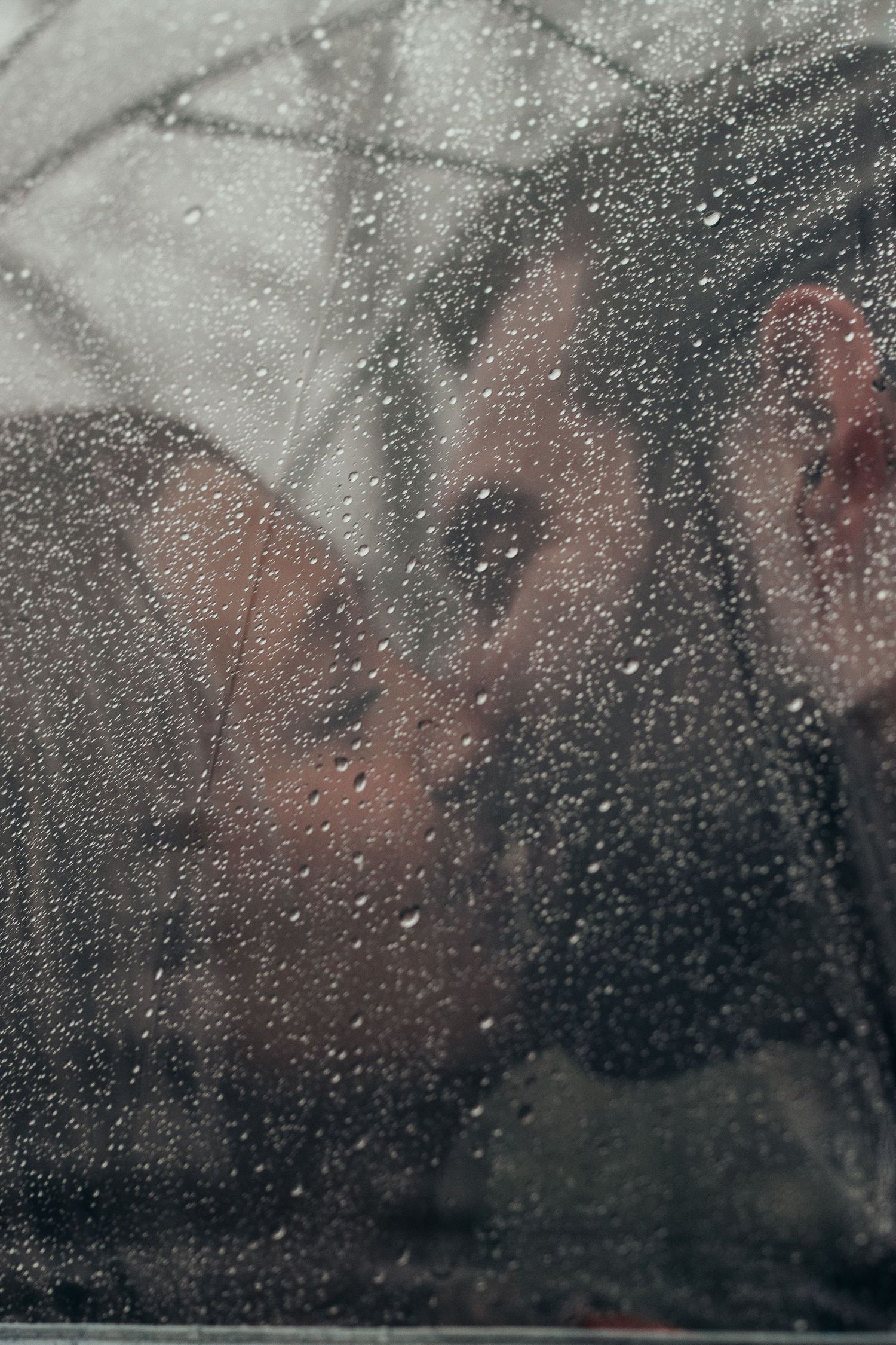 Raindrops on a window creating a moody abstract pattern against a dark background.