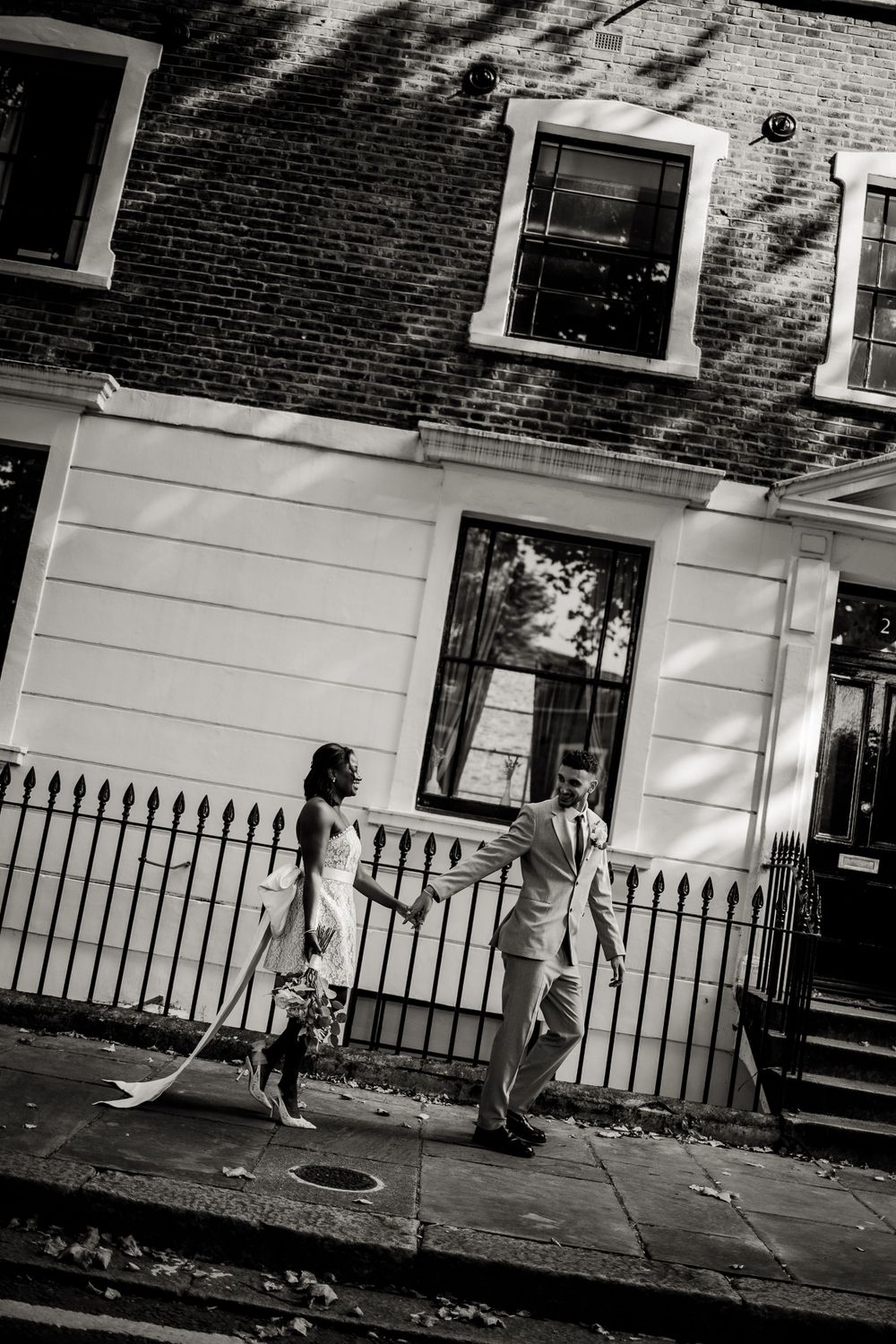 A black and white photo of a couple dancing playfully on a city sidewalk.