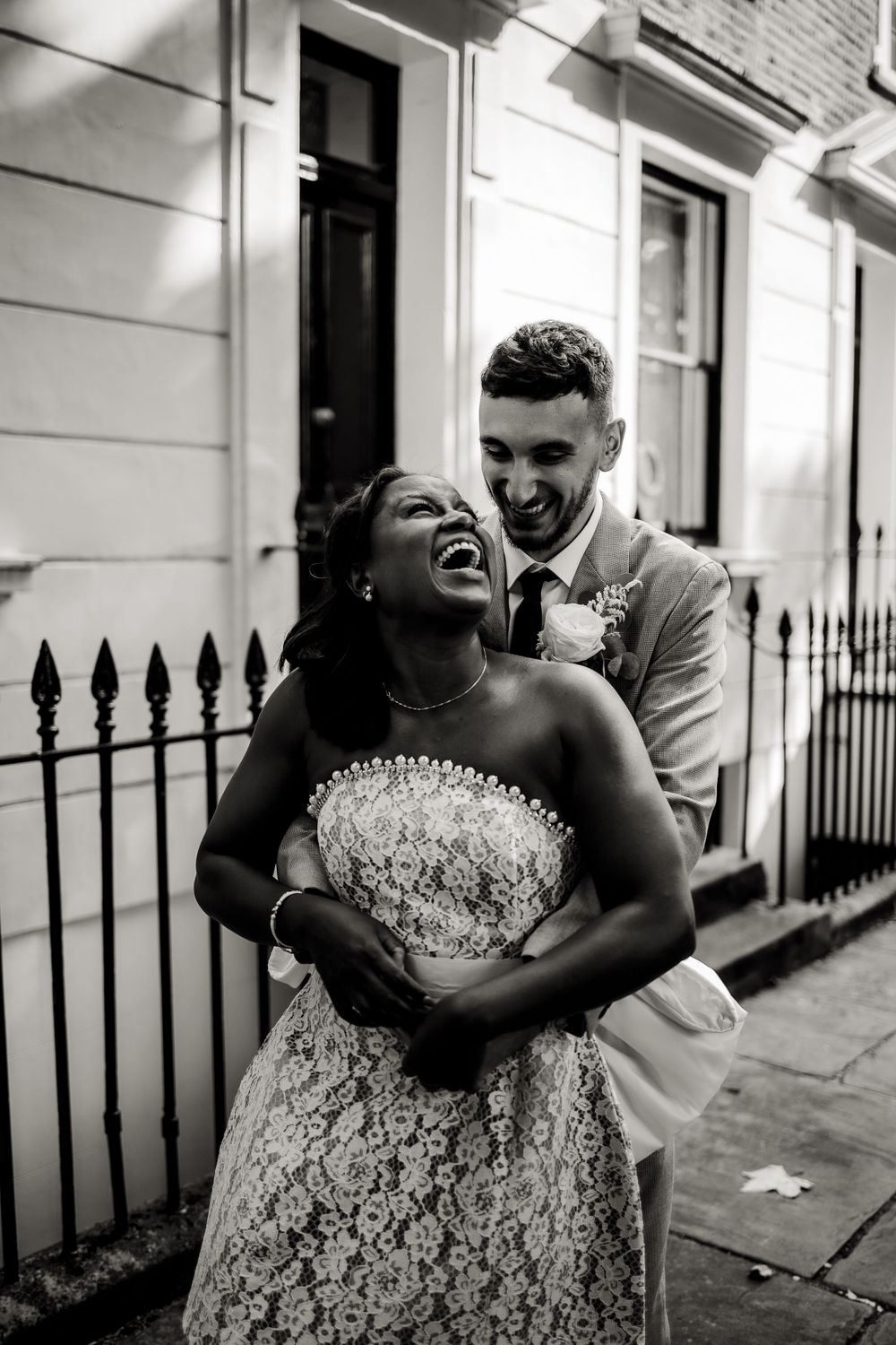 A black and white photo captures a joyful moment between newlyweds by iron railings.