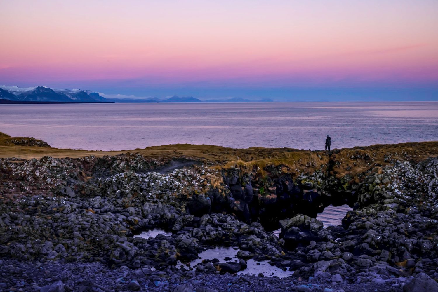 Sally Lombard standing on a natural bridge at the side of the ocean during sunset in Iceland