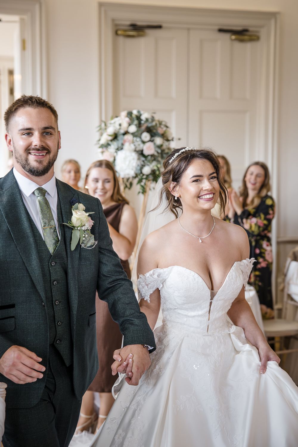 A joyful wedding ceremony moment captured indoors with elegant white floral arrangements and guests in the background.