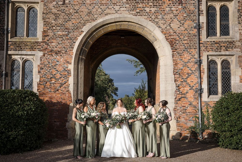 Wedding party poses against historic brick building exterior with arched windows and doorways.