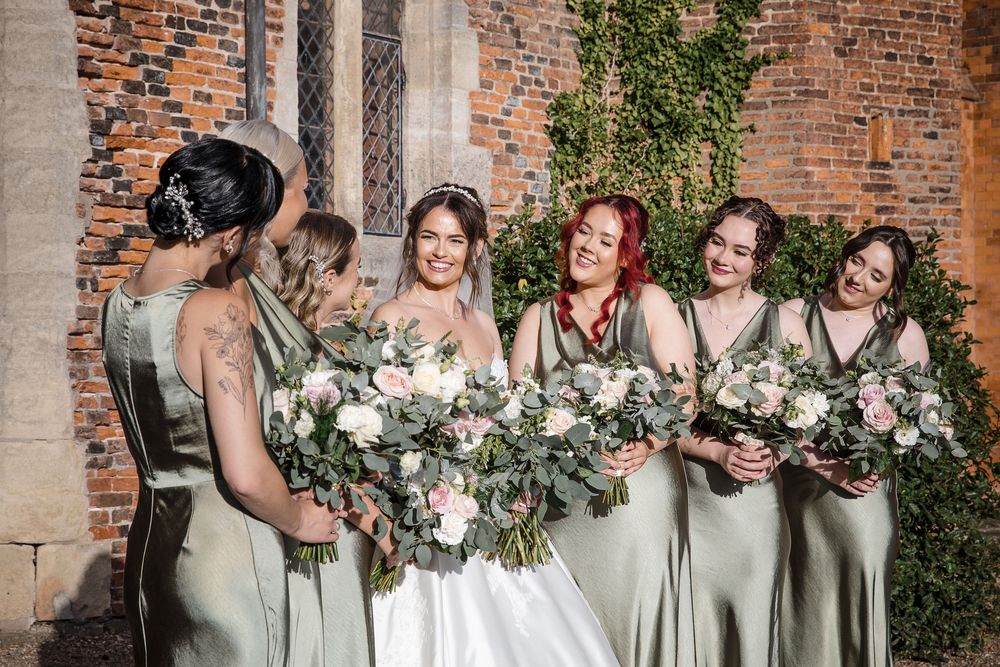 Bridesmaids in sage green dresses stand together at elegant brick venue.