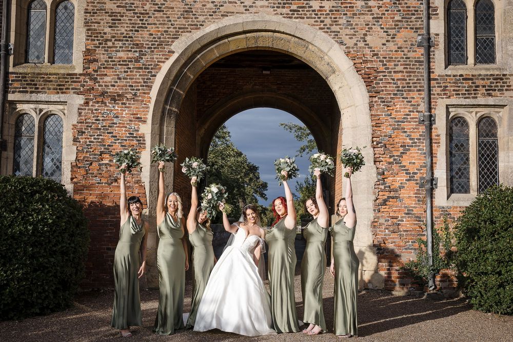 Wedding party poses in front of historic brick building with arched doorway.