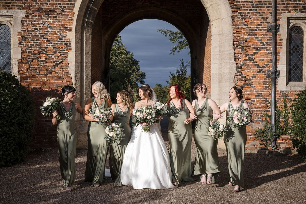 Wedding party poses together in front of historic brick building with elegant archways and columns.
