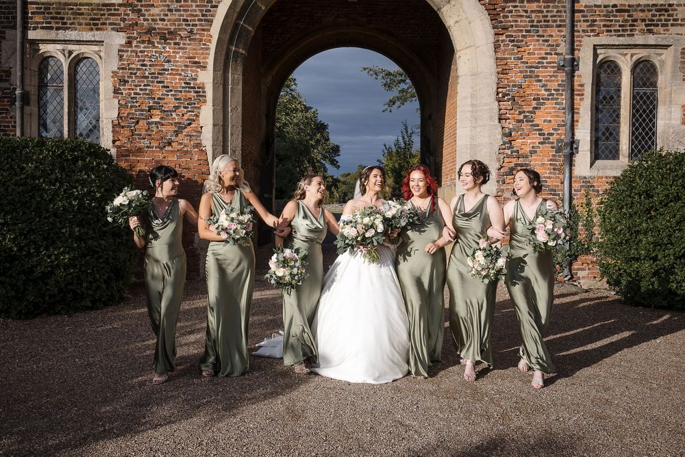 Bridal party in sage green dresses gathered outside historic brick church building.
