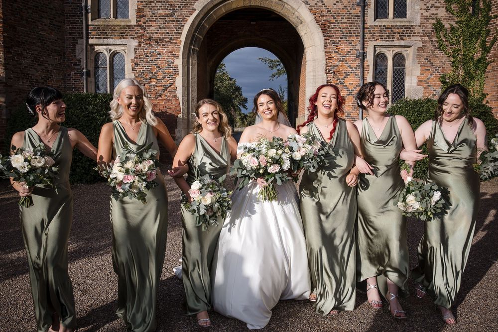 Wedding group gathers in front of rustic brick architecture with arched doorway.