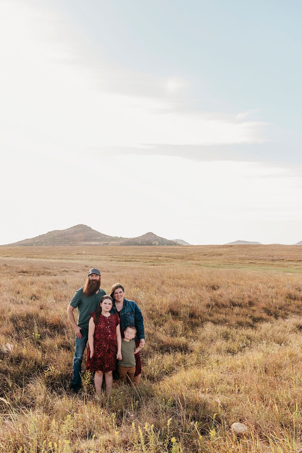 Three friends stand together in a vast golden prairie landscape with mountains visible in the distance.