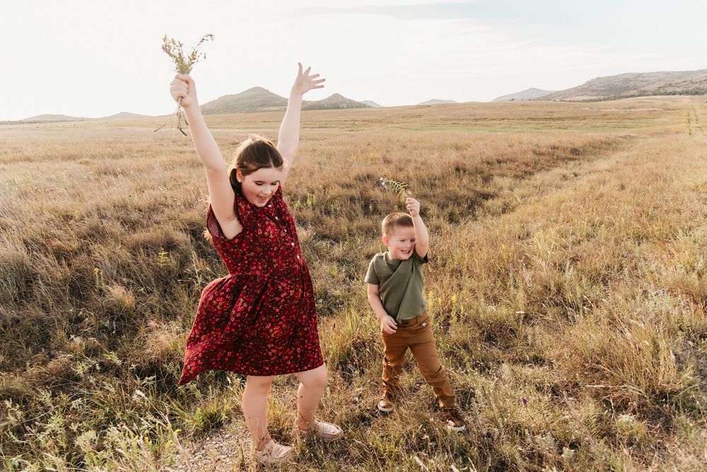 Two people dance and twirl joyfully in a golden field during sunset, creating a romantic outdoor scene.