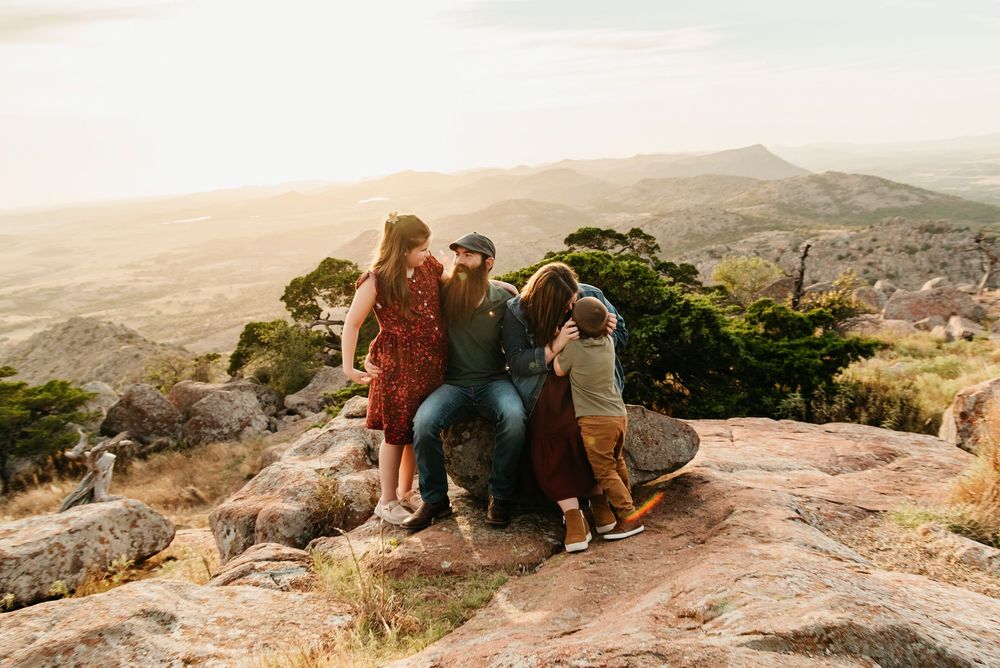 Group of hikers sit at the edge of a scenic mountain overlook during golden hour with expansive valley views below.