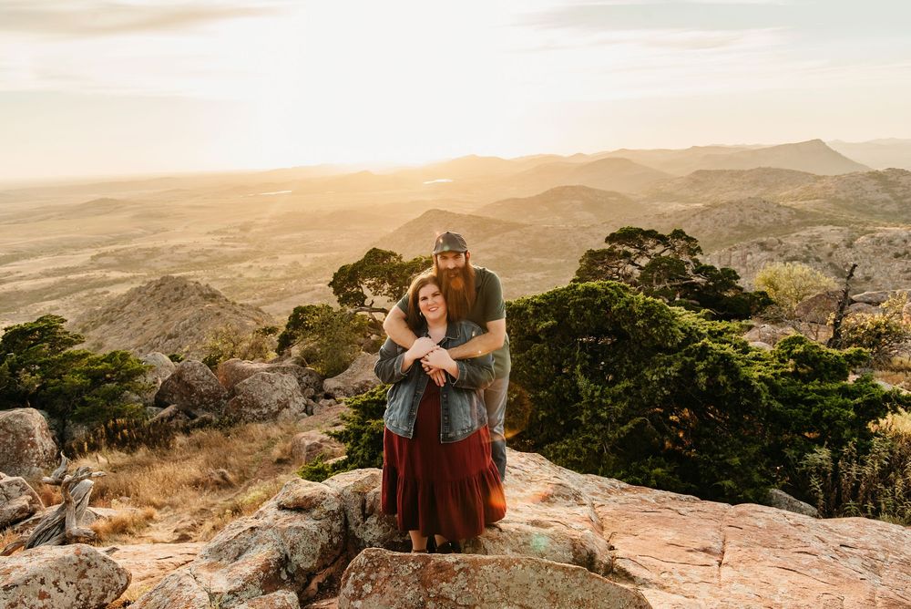 Panoramic mountain landscape view with rocky outcrops and distant rolling hills at sunset.