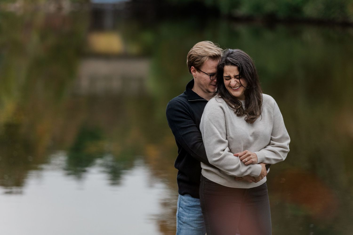 A couple holds hands while walking through an autumn park with colorful fall foliage in the background.