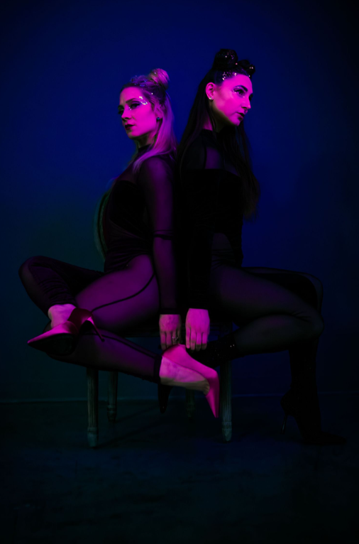 Two silhouetted figures pose dramatically against a dark background with purple and blue lighting effects.