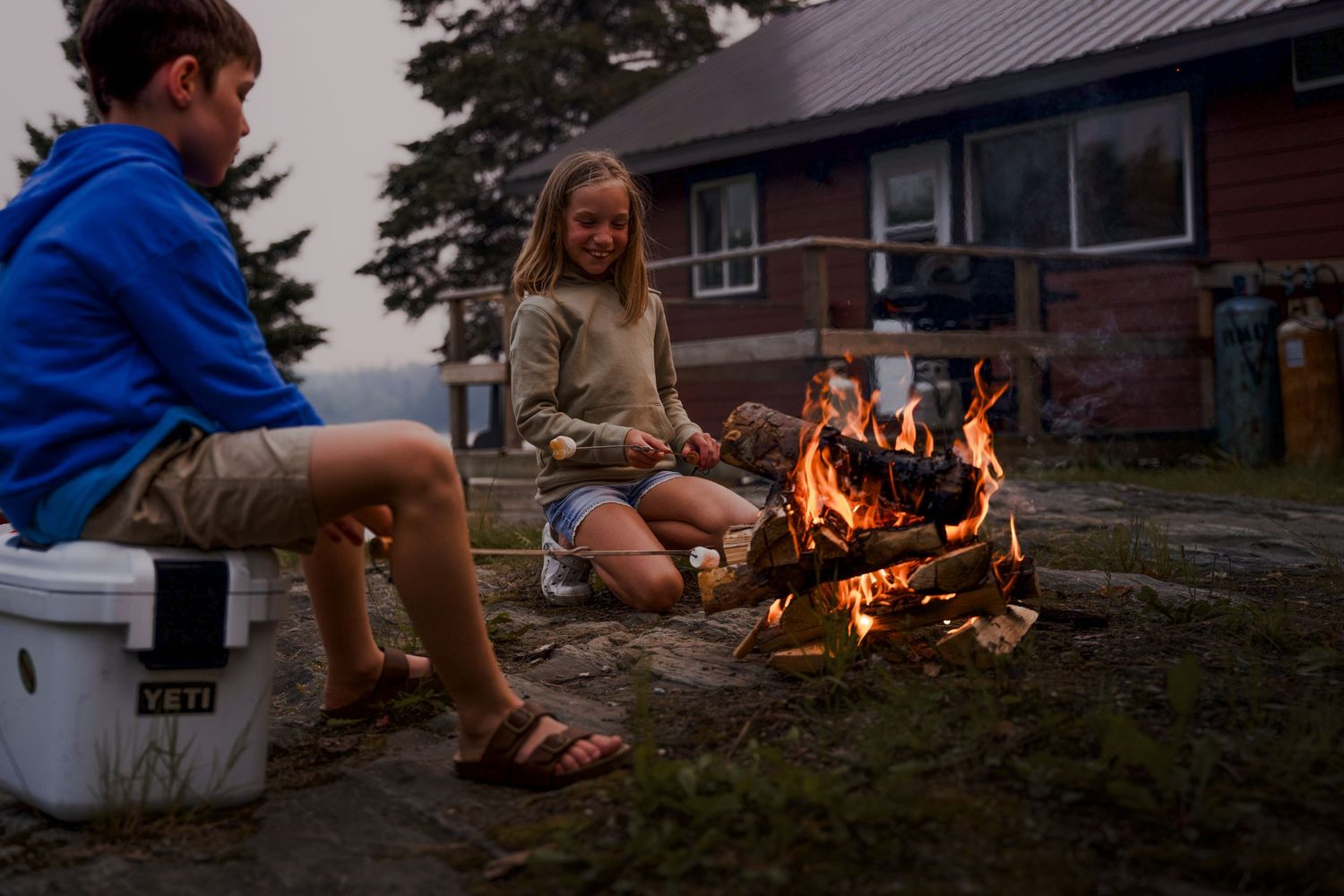 People gathered around a cozy campfire outside a cabin at dusk.