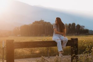 Person sitting on rustic wooden fence at golden hour in countryside setting.
