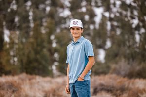 Young person in light blue polo shirt and jeans standing in a natural outdoor setting.