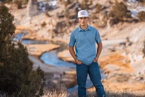Person in blue polo and jeans standing on rocky terrain near winding river.