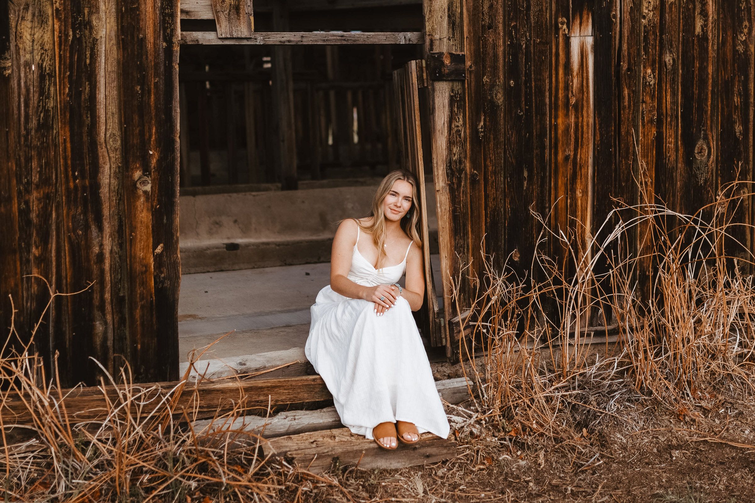 Person in white dress sitting on weathered wooden structure against rustic background.