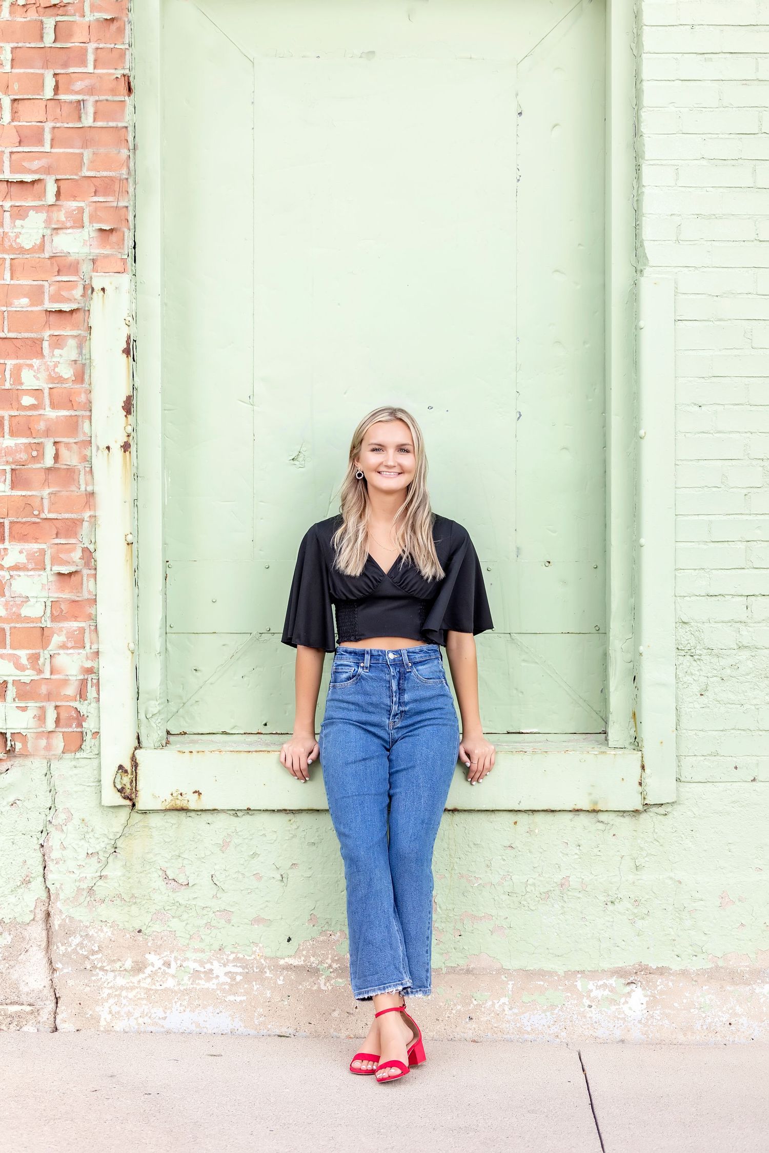 Senior photograph outdoors in Mason City, Iowa featuring mint-green wall and red shoes