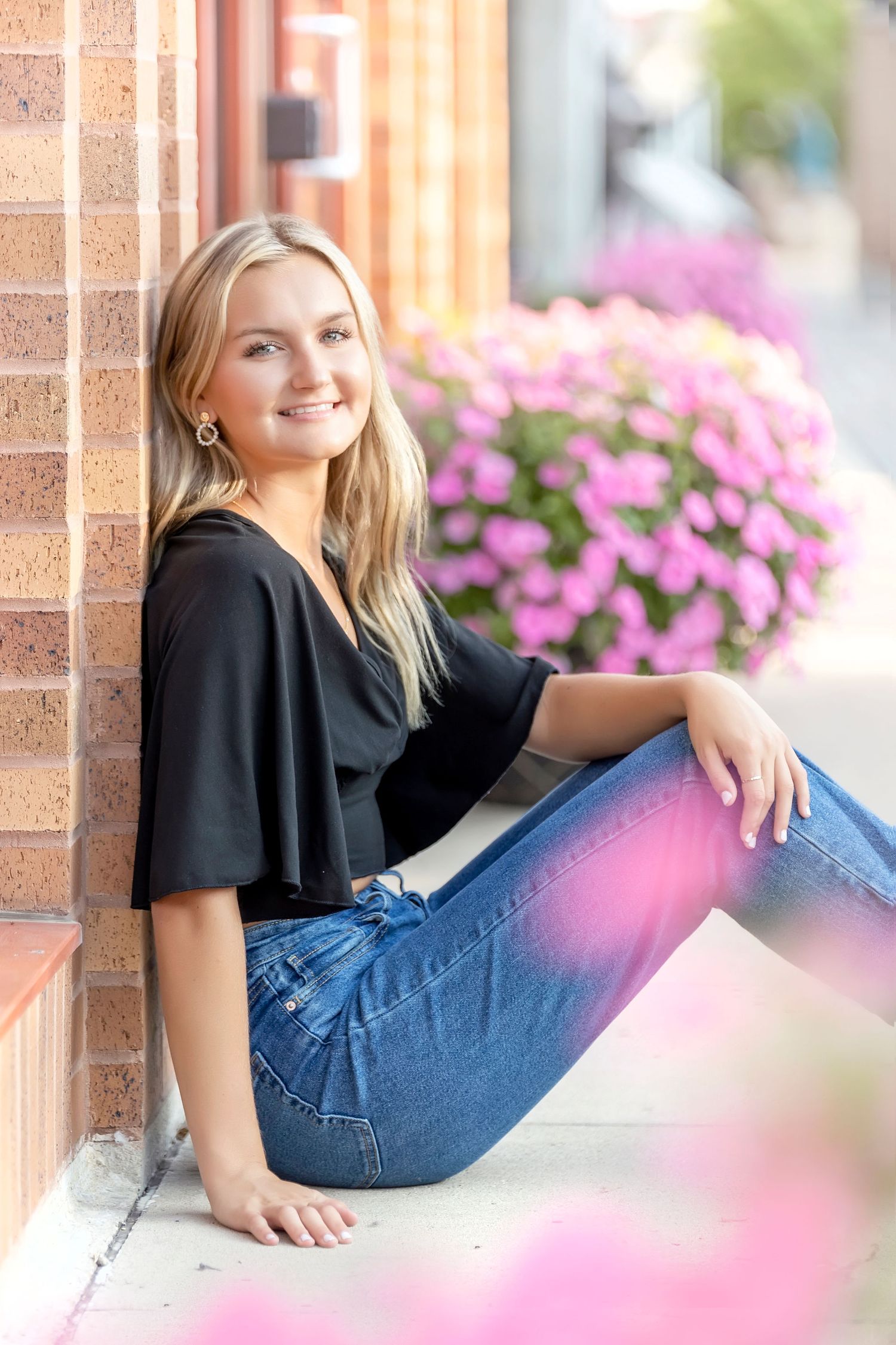 Senior portrait series against brick wall with pink flowers foreground in Mason City senior session