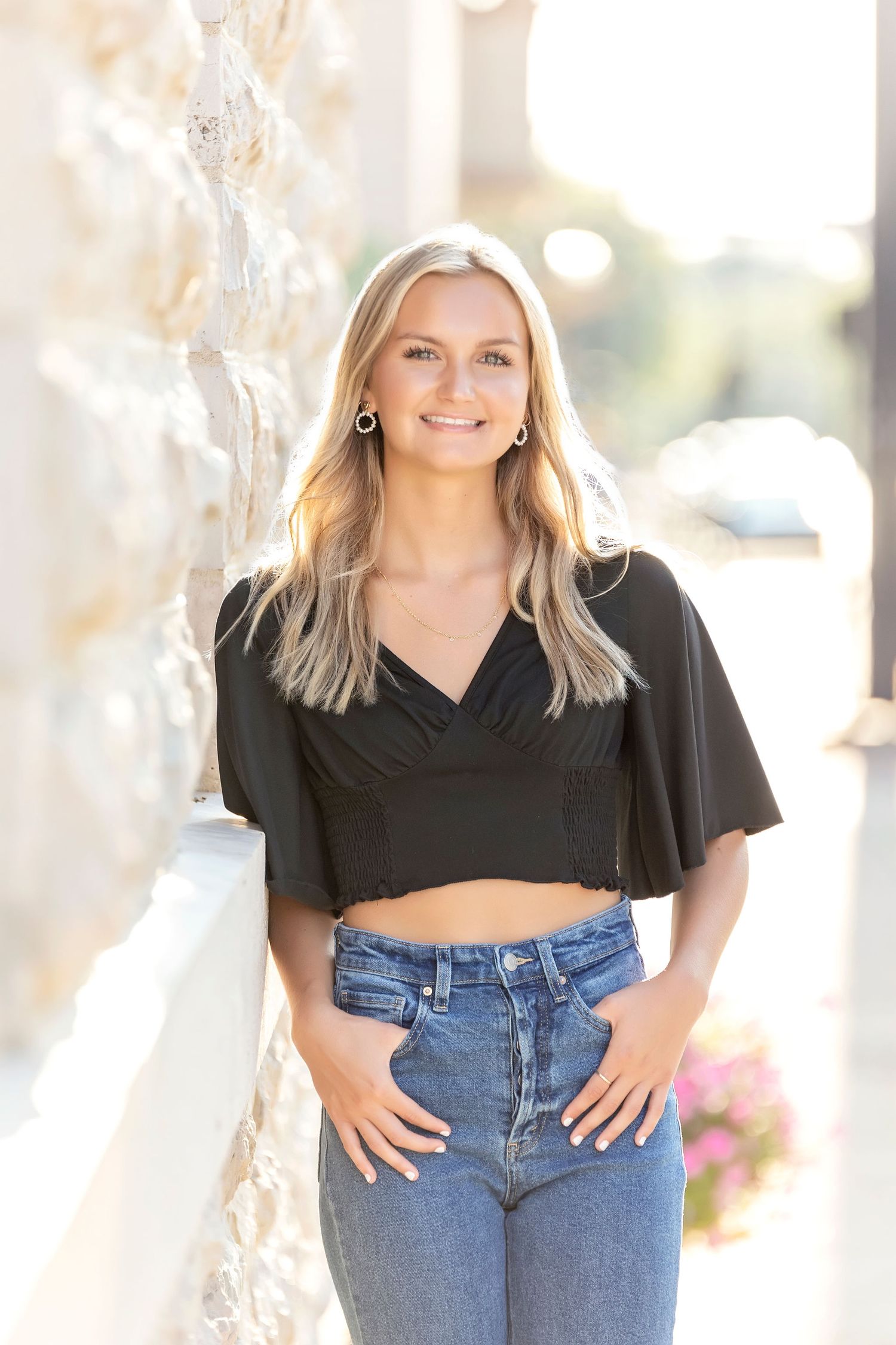 Relaxed senior photo outside of Moorman Clothiers in Mason City in jeans and black top against pale wall with natural light