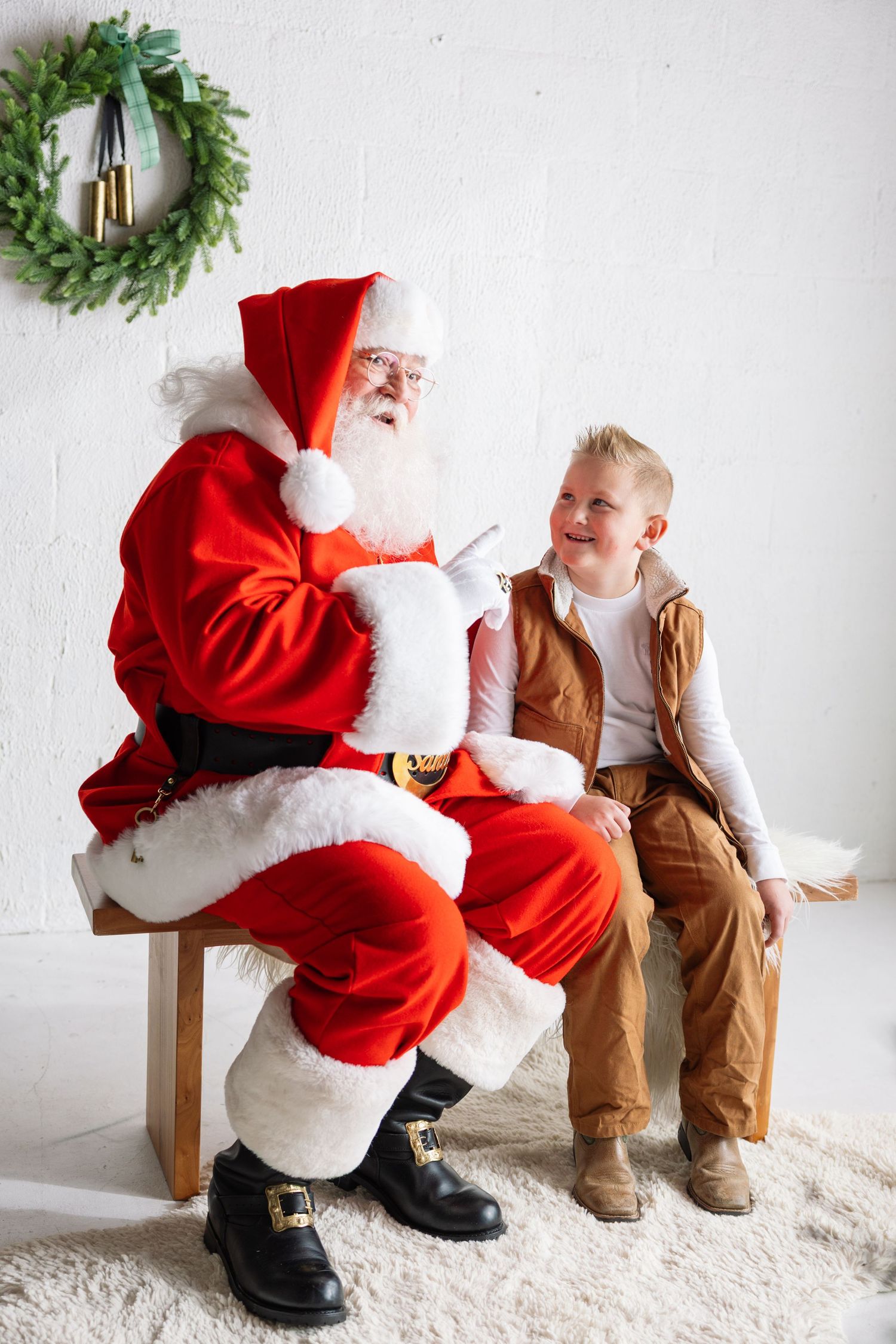 A heartwarming holiday scene with a figure in red and white seated next to a small child in brown overalls.