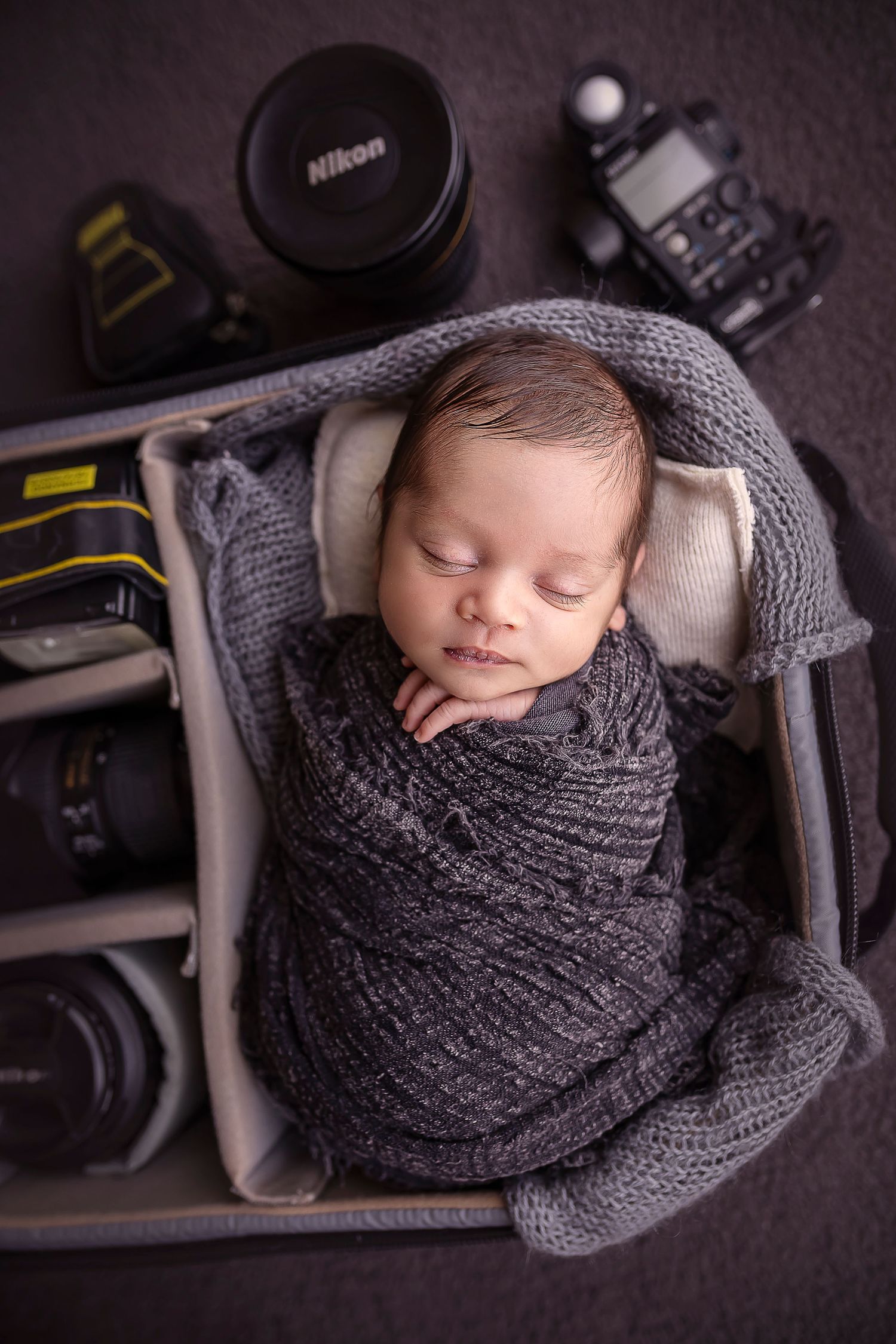 bebe recien nacido posando dentro de un bulto de camara nikon esta envuelto en un pano negro
