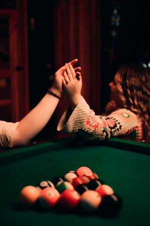 A dramatic pool table shot showing billiard balls and hands in moody red lighting.