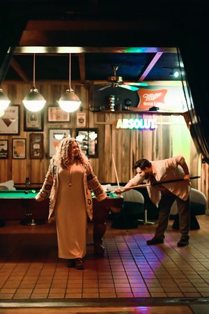 A sequence of dance moves shown on a tiled floor in a bar with wood paneled walls and neon lighting.