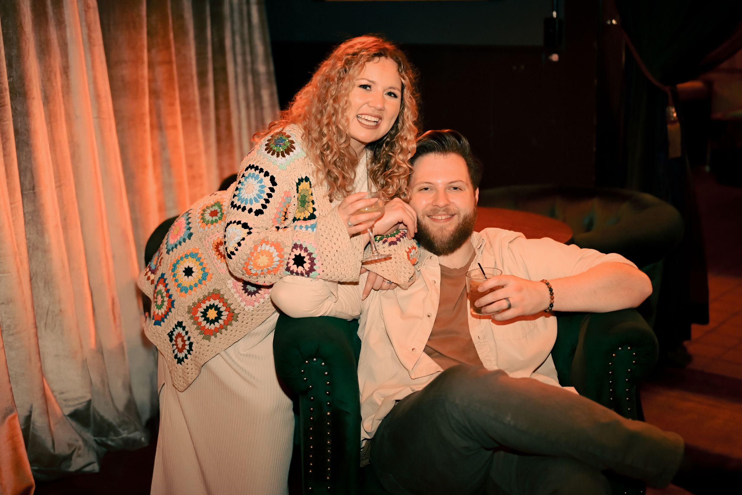 A couple relaxes together on a couch in warm lighting, with one wearing a patterned sweater.
