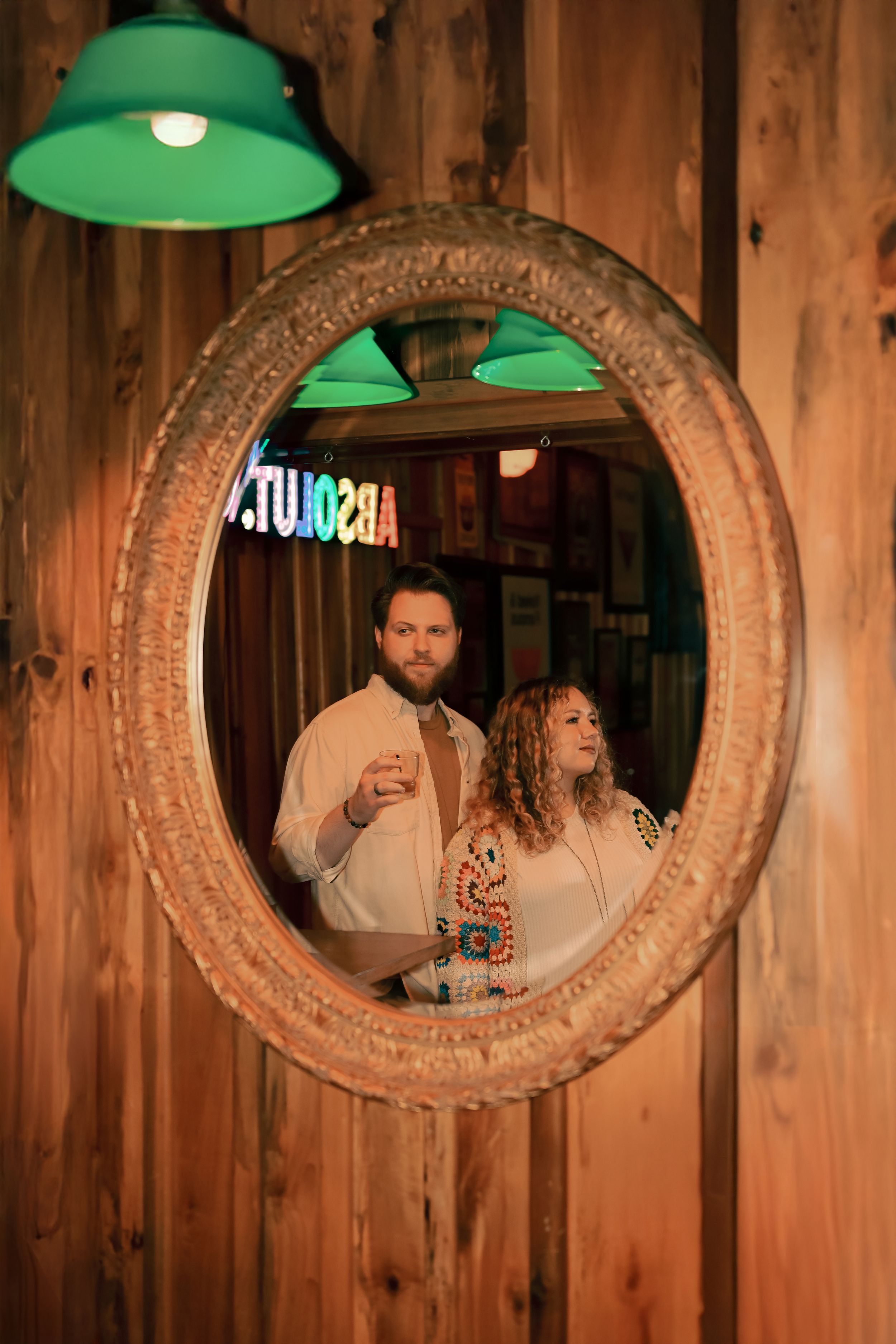 Artistic photo series showing people through round vintage mirror frames mounted on wooden wall with green lighting.
