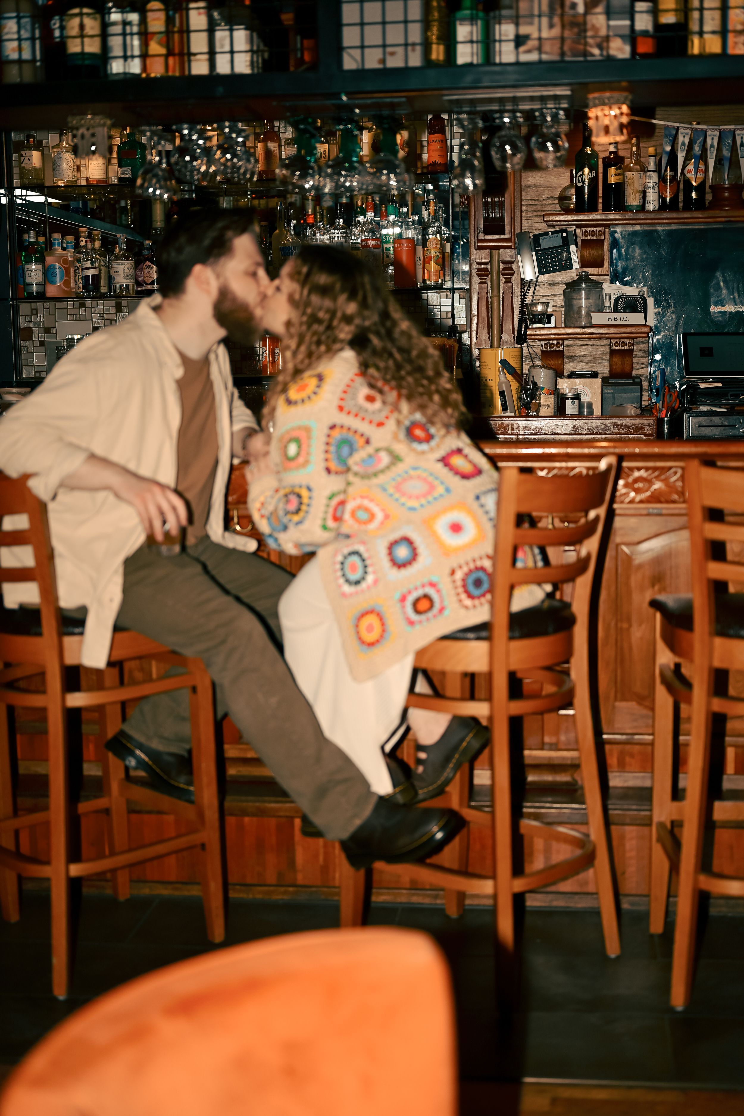 A person in a patterned sweater falling backwards off a wooden bar stool in a dimly lit pub setting.