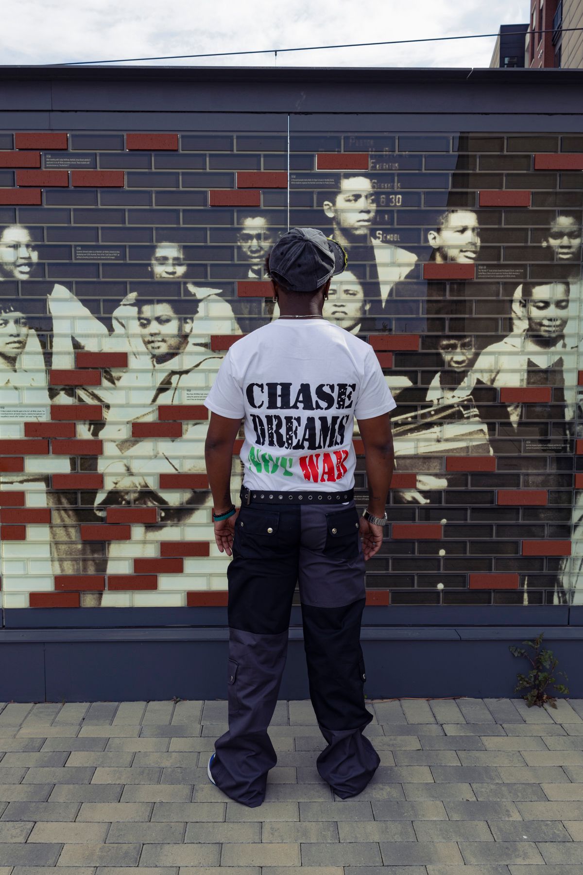 Person wearing Chase Dreams shirt viewing historical mural on brick wall.