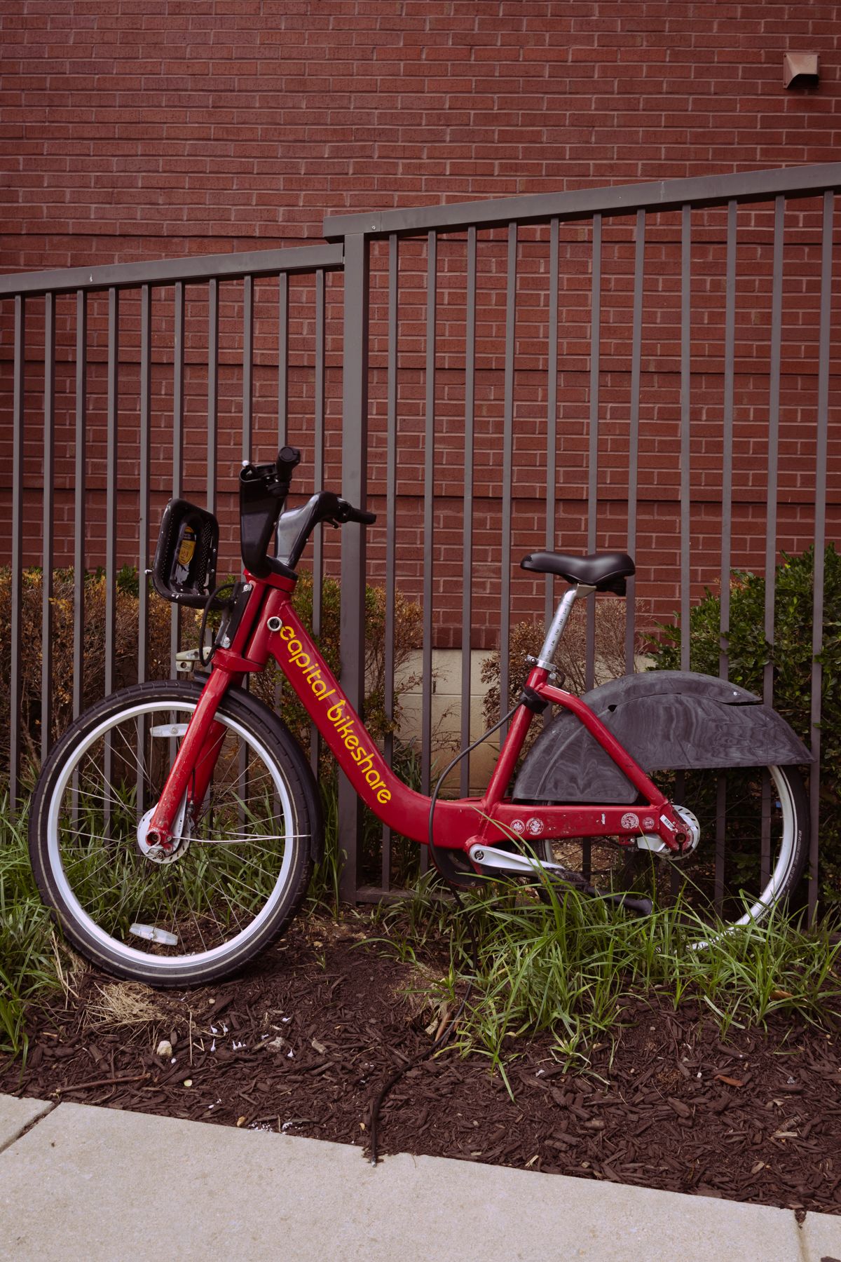 Red bicycle lying on its side against a brick wall with metal railings.