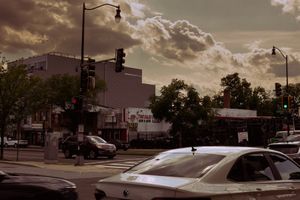 Dramatic cloudy sunset sky over an urban street with parked cars and buildings.