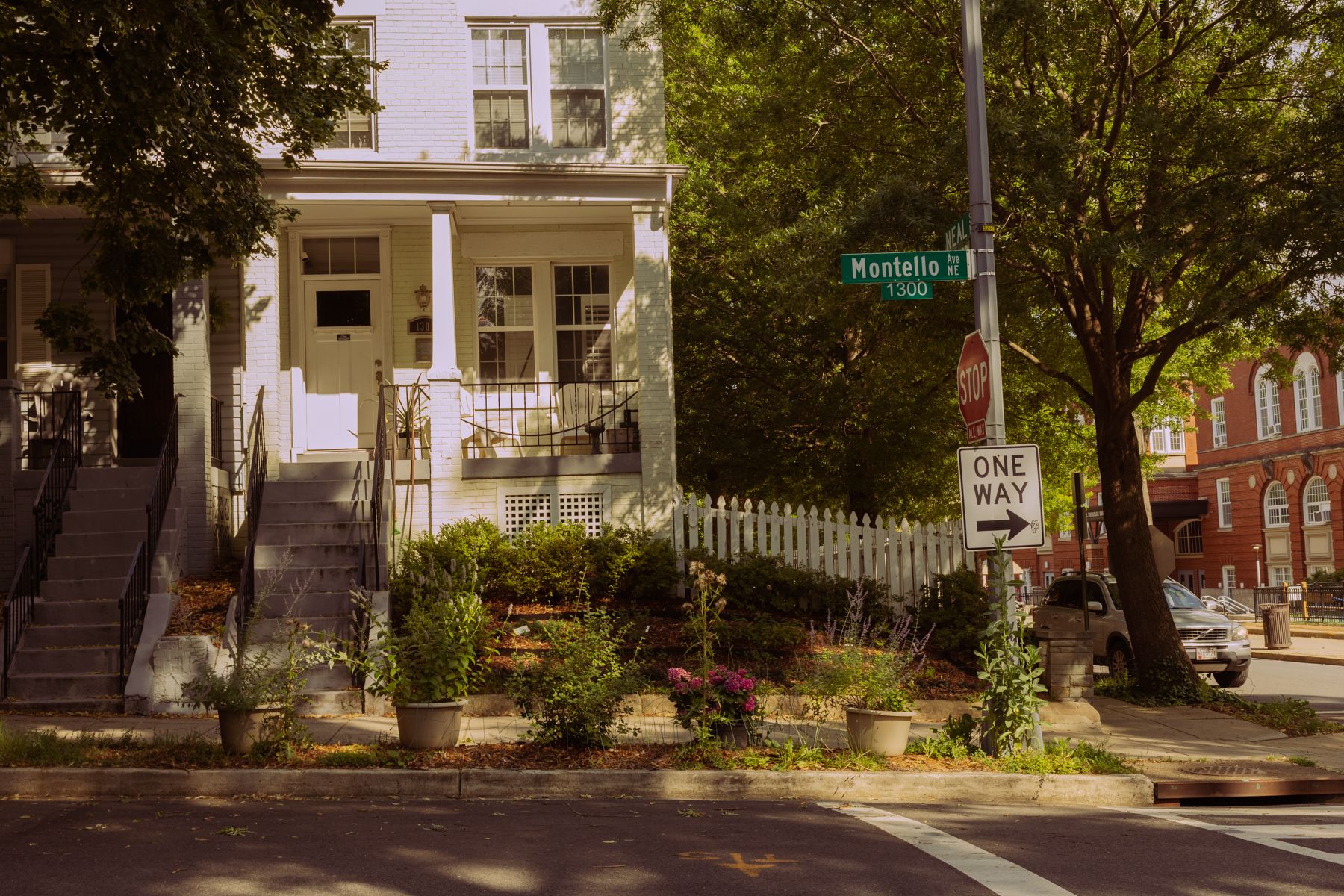 Row of historic brownstone houses with white trim and porches on a tree-lined residential street.
