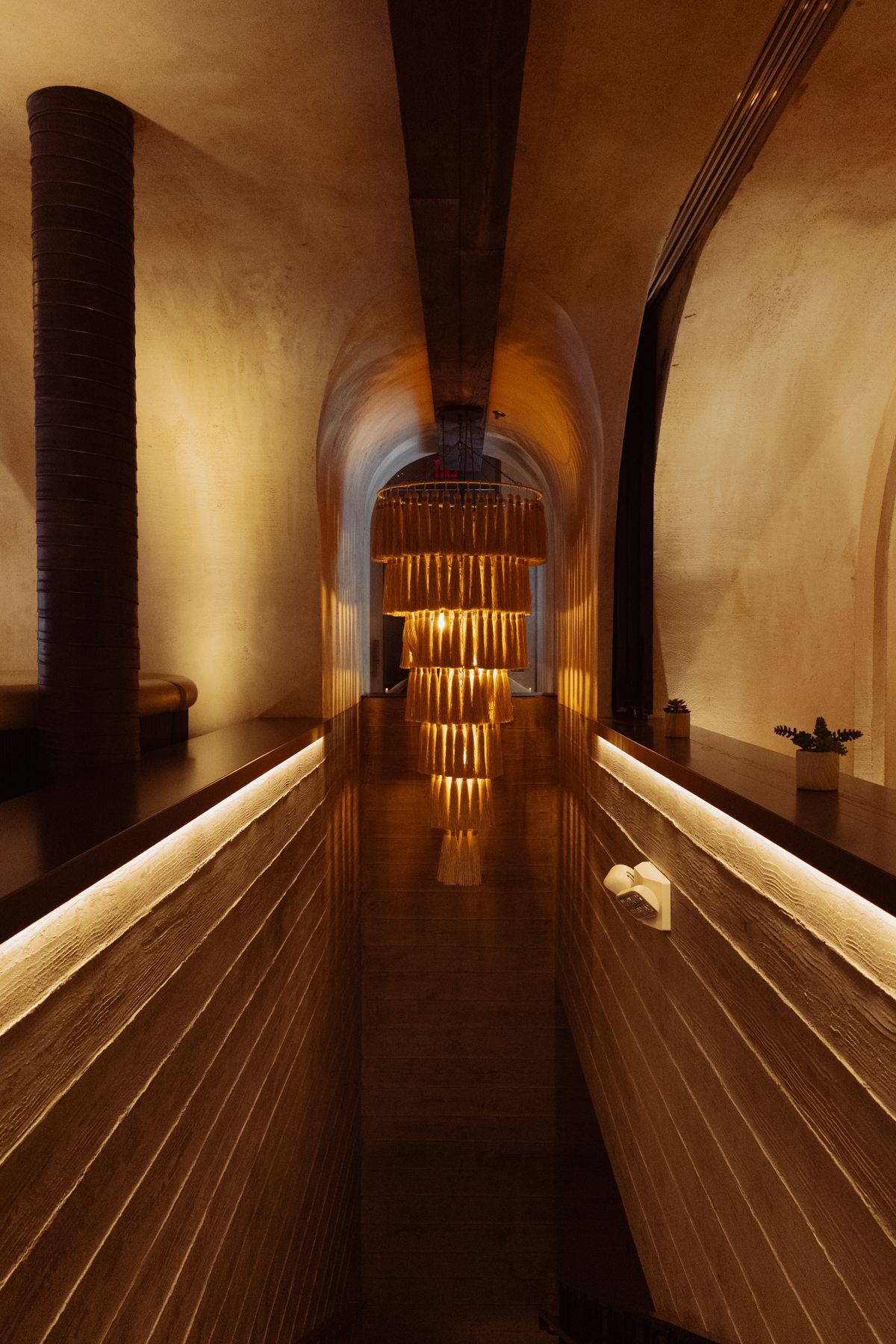 Long wooden hallway with arched ceiling and dramatic lighting creating geometric patterns.
