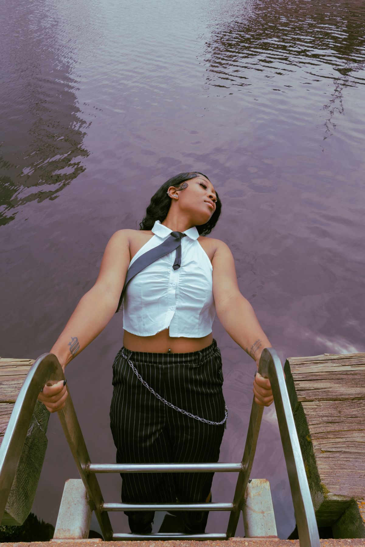 Person relaxing on wooden dock stairs over purple-tinted water on a calm day.