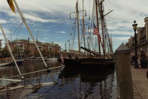 Historic sailing ships docked at a waterfront marina with cloudy skies overhead.