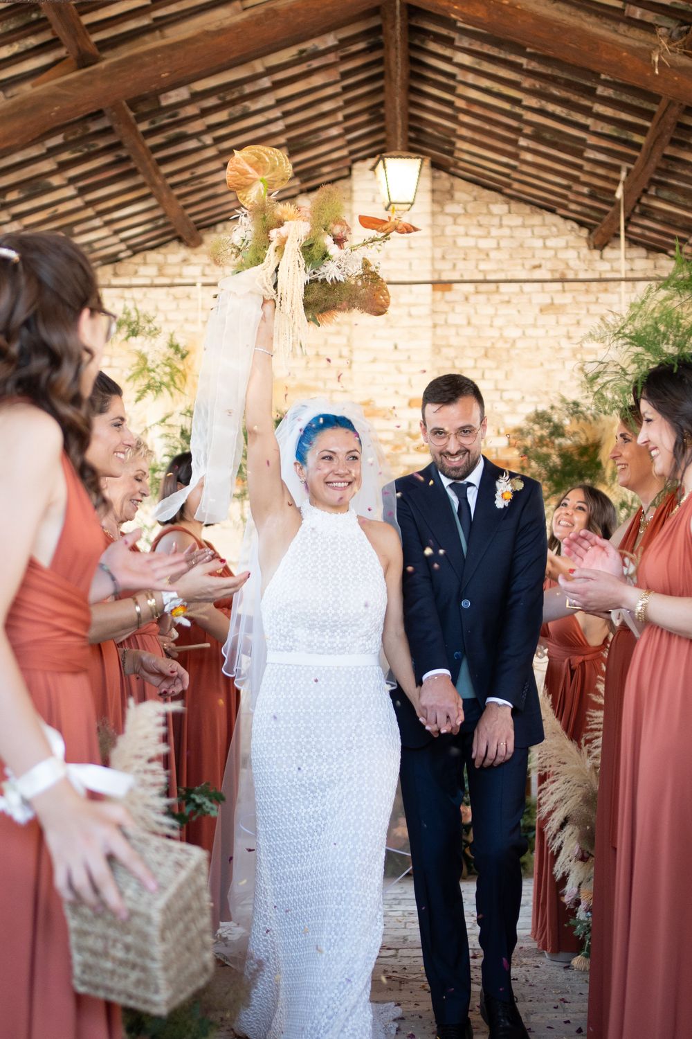 Wedding party celebrates in rustic brick venue with bridesmaids in coral dresses and bride in white lace dress.