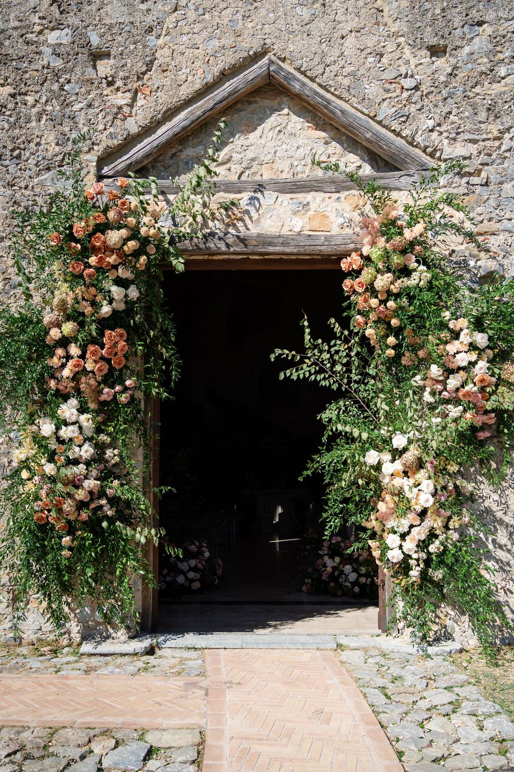 Rustic stone archway entrance adorned with climbing roses and peach flowers creating a romantic garden entryway.