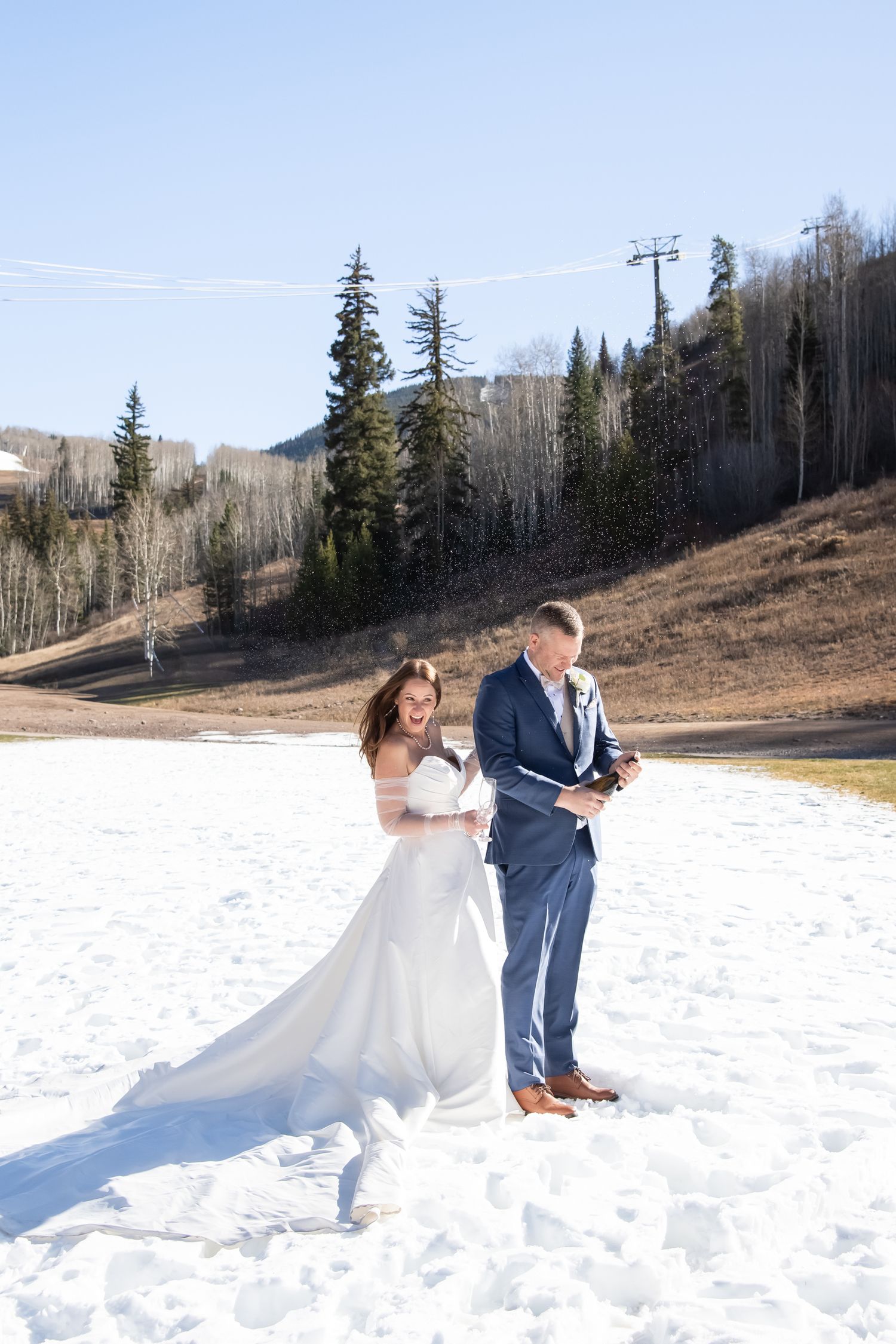 Elegant bride and groom pop a bottle of champagne in the snow after their micro wedding at The Beaver Creek Chapel