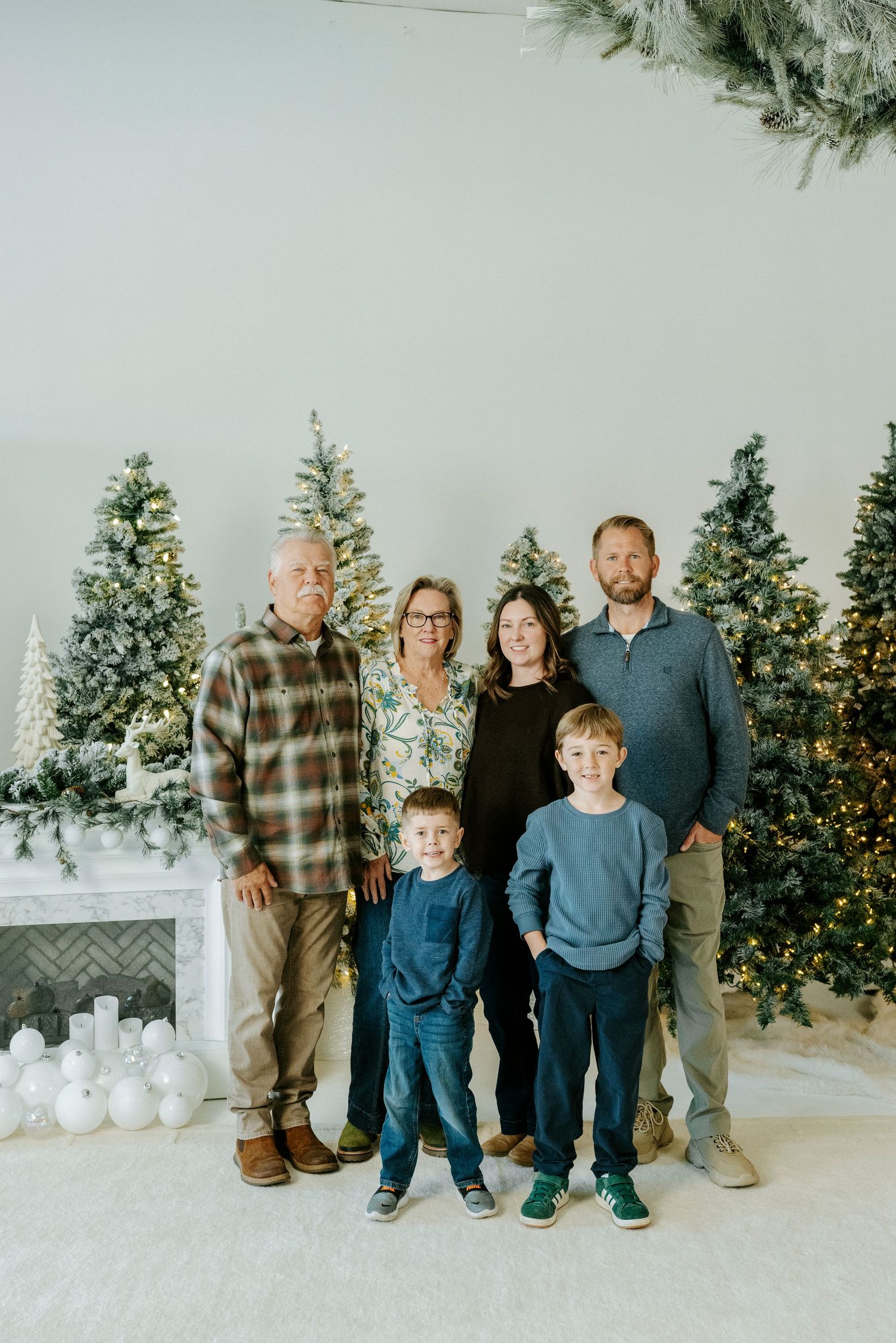 A family poses together in front of a decorated Christmas scene with evergreen trees and white winter decor.