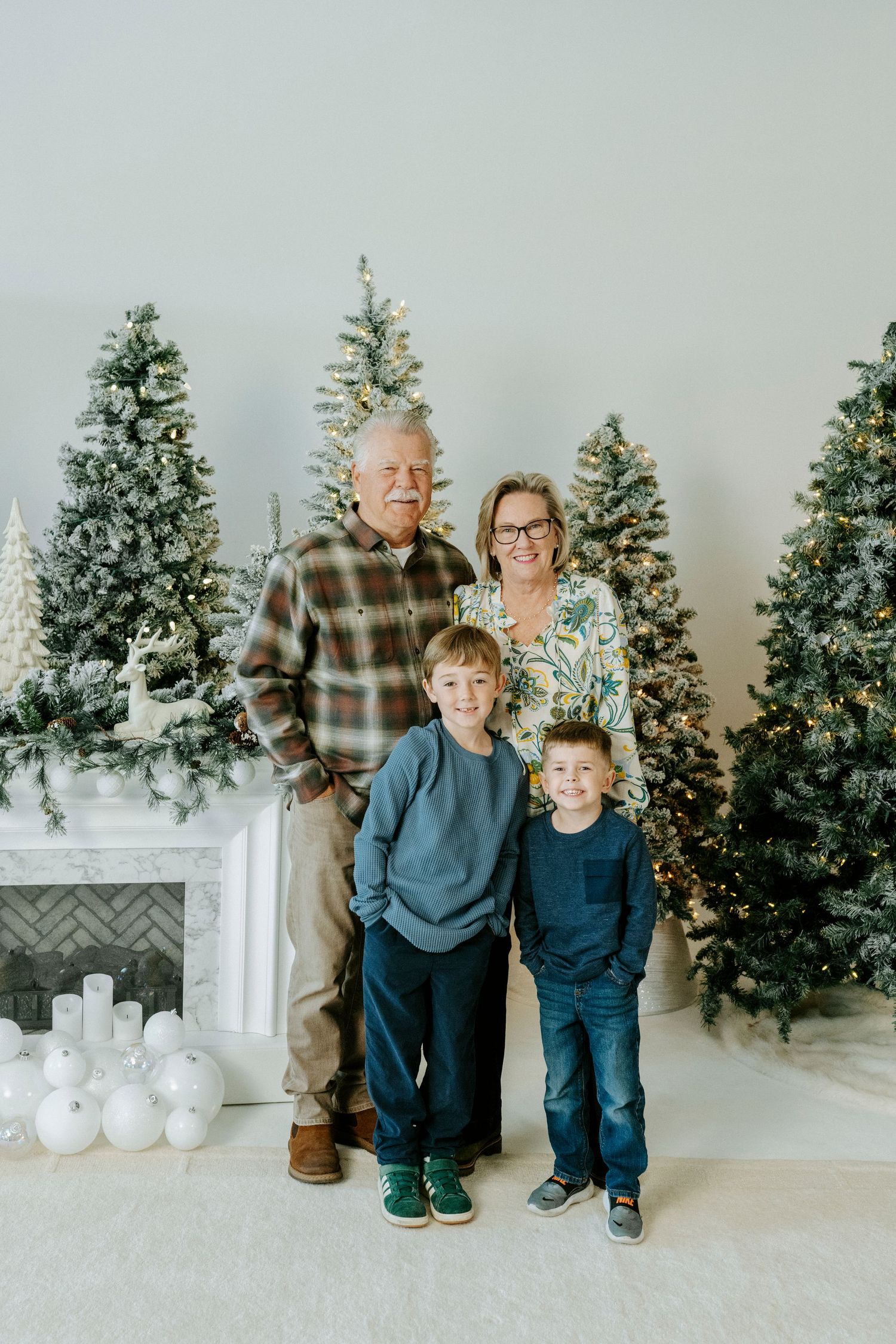 Holiday photo session setup with decorated Christmas trees, white fireplace mantel and silver ornament decorations.